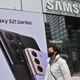 A woman walks by in front of a Samsung store and an advertisement for the Samsung Galaxy S21.